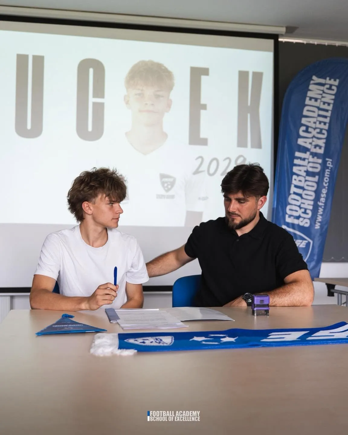 Zawodnik podpisuje dokumenty przy klubowym banerze FASE