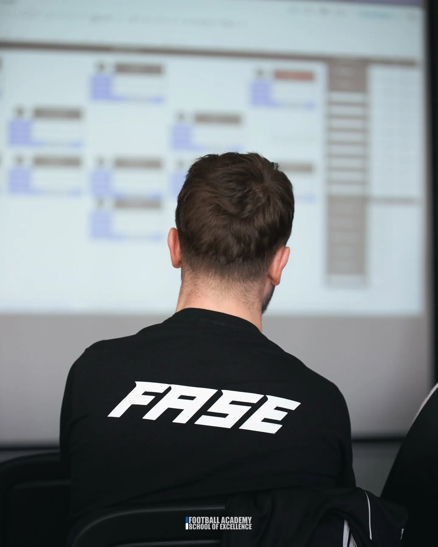 Trener w bluzie FASE przed ekranem z analizą podczas odprawy sztabu